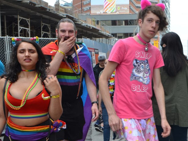 a young man with pink t shirt and fuzzy pink ears, another man with a rainbow flag on his back and his hand over his mouth 