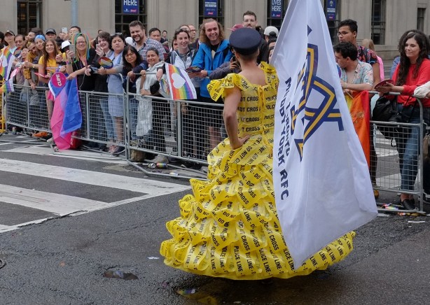 a man wears a dress made of yellow police caution tape in a parade 