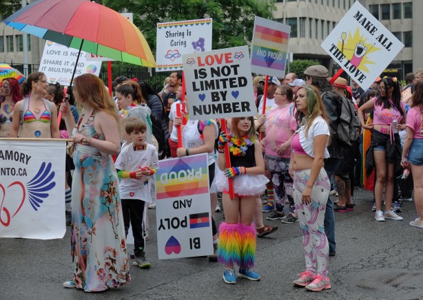polyamory group, men, women and children, with colourful clothes and signs waits their turn to join the pride parade 