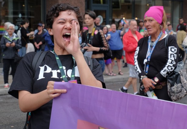 a young woman in black Pride T-shirt, holds a purple banner and is yelling dyke march 2018