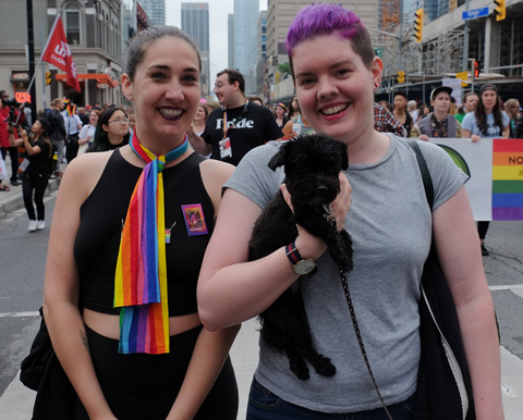 dyke march 2018 - two women in the parade, one with short purple hair, carrying a small black dog 