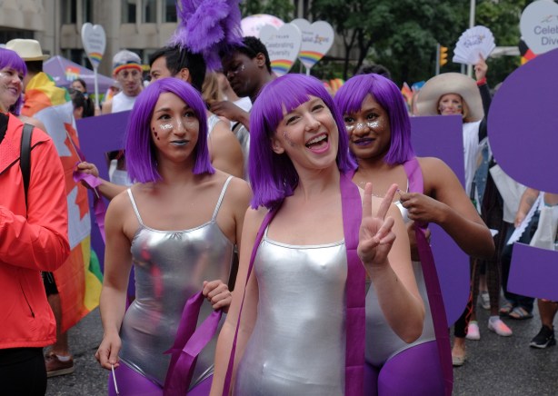 three women wearing tight silver bathing suits and purple wigs