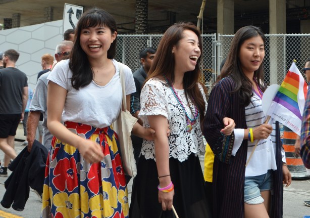 three Asian woman laughing as they walk down the street, looking at something that has made them laugh 