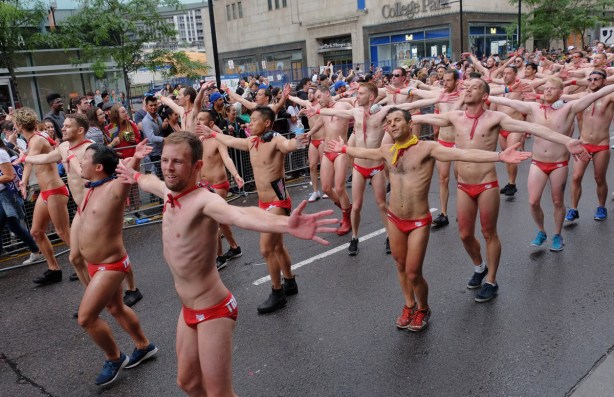 trigger fish waterpolo team parades in their red swim suits, dancing to music, arms out at their sides, passing in front of College Park building