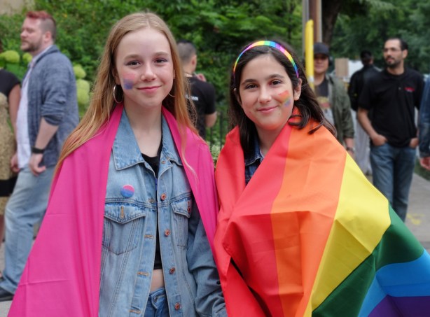 watching the dyke march 2018 - two girls on Yonge street draped in rainbow flags 