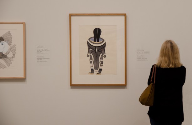 woman in an art gallery looking at two pictures on the wall, both by Kenojuak Ashevak 