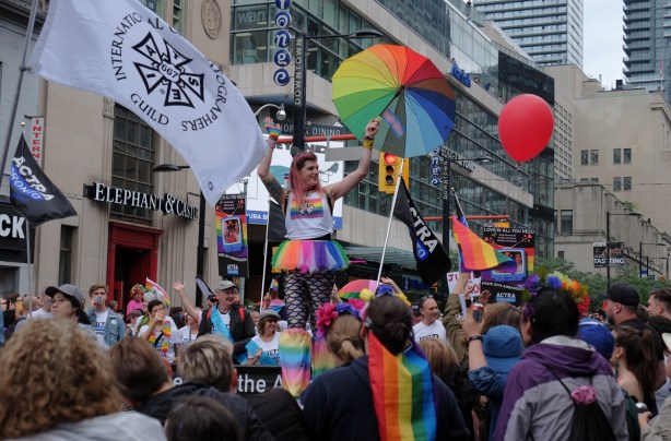 a woman on stilts carries a rainbow umbrella as she walks with iatse group in the pride parade