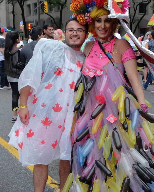 a man in a rain pncho covreed with red maple leaves is posing with a man dressed in a dress that is covered with condoms 