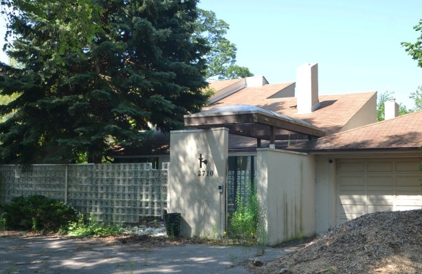 modern style house with glass brick wall in front, around a front porch, large spruce tree, overgrown driveway, 