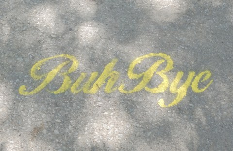 yellow stencil on a sidewalk, in cursive writing, buh bye 
