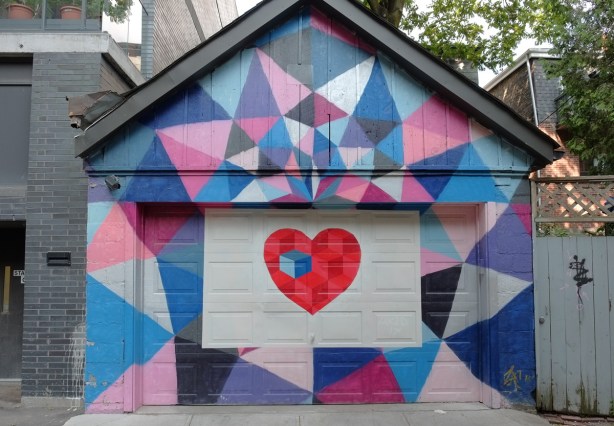 garage and garage door painted in mural with a red heart in the center, surrounded by pink, purple and blue triangles 