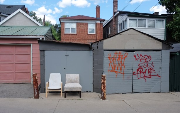 two comfy chairs in an alley withtheir backs agains a grey garage door