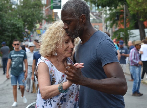 a black man dances on the street, slow dance, with an older blond woman, 