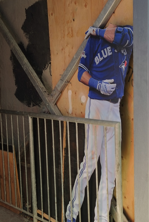 a headless cardboard cut out of a Toronto Blue Jay baseball player, in a doorway, in a lane. 