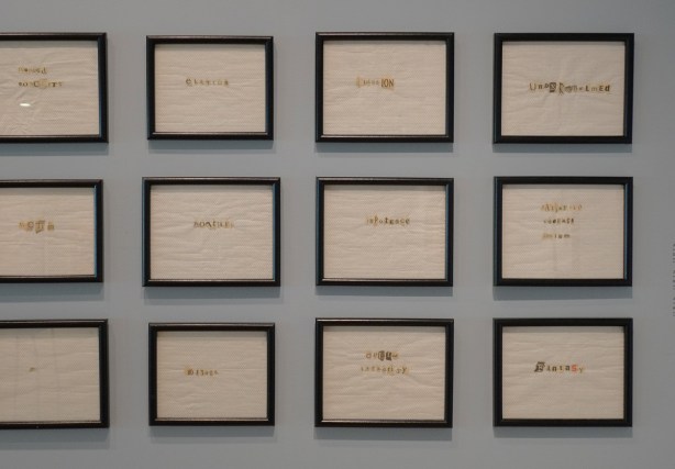 a grid of 8 square artworks by June Clark on a gallery wall - black frames around pieces of paper towel with words on them formed from cut outs from newspapers,