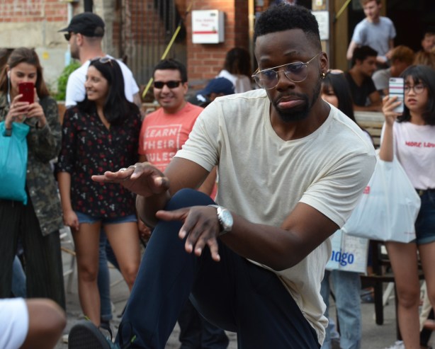 young black man dancing on the street, part of a group, Pedestrian Sunday afternoon at Kensington, people in the background watching 