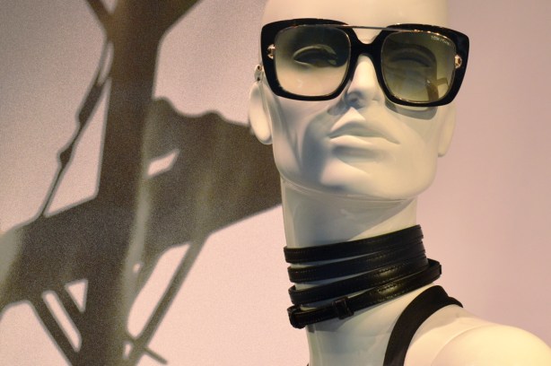 head of a mannequin in a store window, white, large sunglasses, leather rings around her neck 