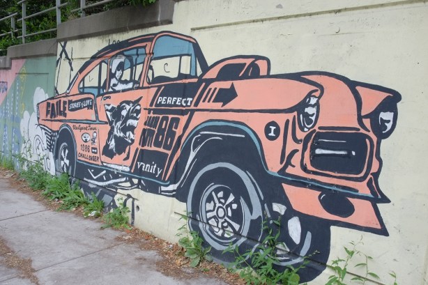 mural, by faile, orange car, woman driver, the word vanity written on the side of the car