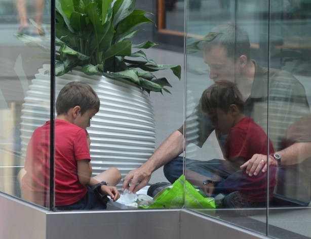 a man sits with his son on the floor of the Eaton Centre, next to the glass railing. reflections from the railing make it look like there are two boys 