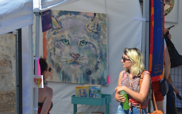 a woman walks past a painting of a cat head in blues and greys, 