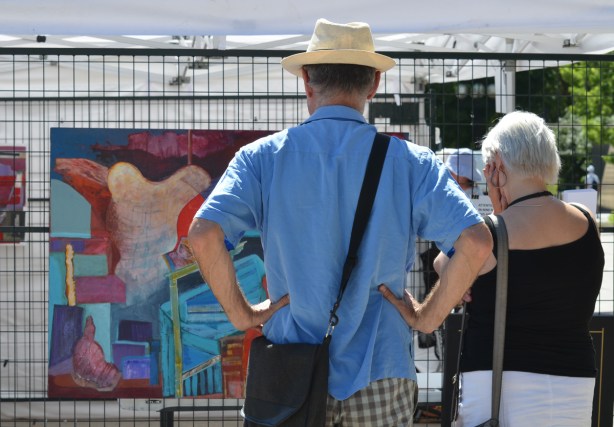 a couple looks at a painting at an outdoor art fair 