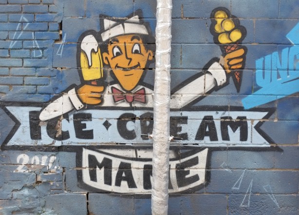 street art painting in a laneway of a man in white uniform and hat, holding popsicle in one hand and ice cream cone in the other, words say ice cream mane