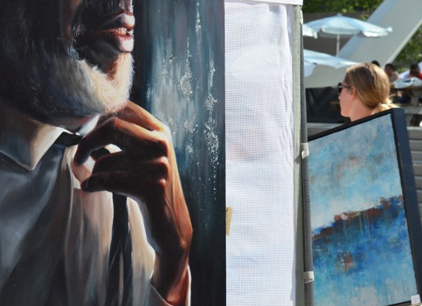 a woman carries a large painting, passes by another large painting of a black man with a white beard 