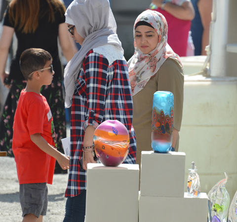 two muslim women in head scarves walk past some glass sculptures at an outdoor art fair 