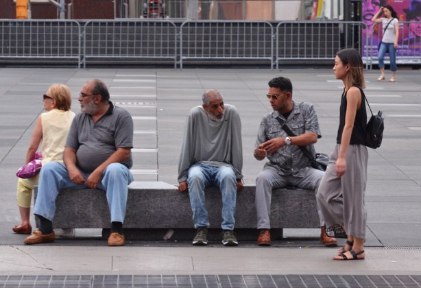 men sitting on a bench, a woman walking past 