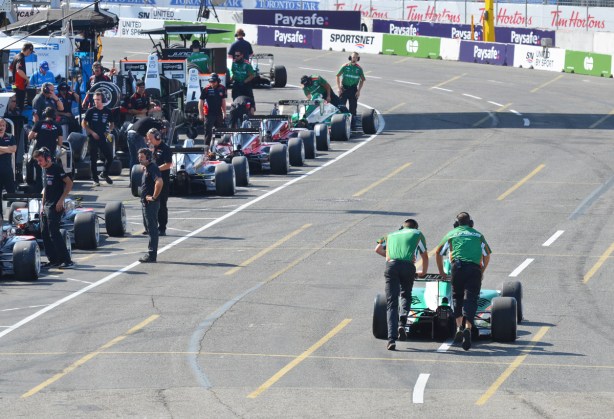 two men in green shirts push a race car to its position in the pit lane, Honda Indy, Toronto