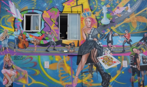 large mural on the side of a building in an alley, theme is Queen Street west, queen of hearts heart, musicians, 