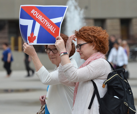 two middle aged red headed women holding a sign at a protest at city hall 