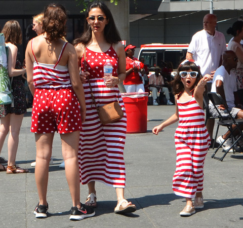 a greoup of three people in red and white clothes st Yonge Dundas square for Canada Day, a girl in a red and white striped long dress and two women in red and white polka dots and stripes 