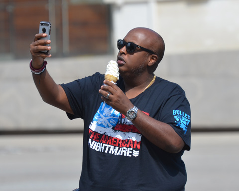 bald black man with black sunglasses is taking a selfie while holding a large ice cream cone