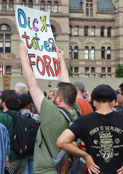 a man in a green t shirt holds up a protest sign that says Dick-tator Ford 