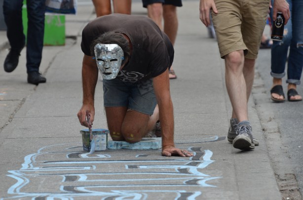 victor painting on the sidewalk in Kensington.  He's wearing a shiny sparkly mask over the top of his head. people are walking past #whatsvictorupto