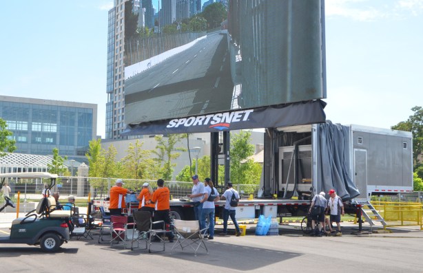 large TV screen mounted on a metal post outside the back of a truck, mobile TV network setup to cover the Indy. picture on screen is of part of the racetrack. 