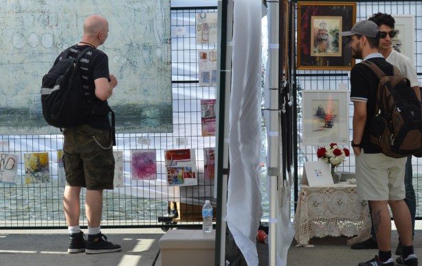 three men, in two different booths, side by side, looking at paintings, Nathan Phillips Square, outdoor art fair 