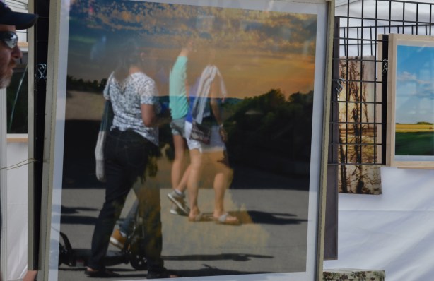 reflections in a framed artwork, people passing by, outdoor art fair 
