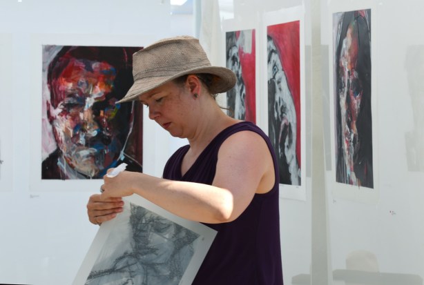 woman in a brown hat starts to pack up her paintings of people's faces at the end of an outdoor art fair in Toronto 