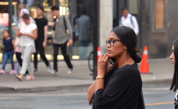 a woman on the sidewalk, with people on the other side of the street in the background 