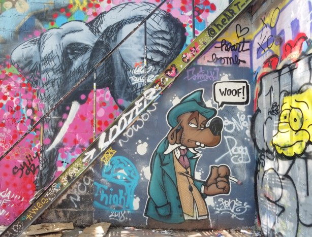 graffiti above and below a diagonal metal staircase, an elephant above the stairs and a dog below. The dog is saying woof 