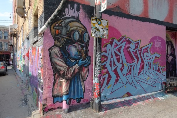 a mural of a person in an old fashioned aviator's helmet and goggles, and wearing a blue dress, on a door in an lane 