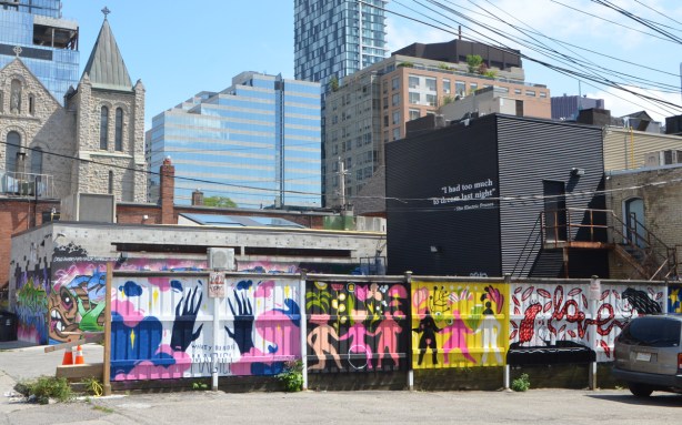 fence with murals painted on it, large buildings behind it, 