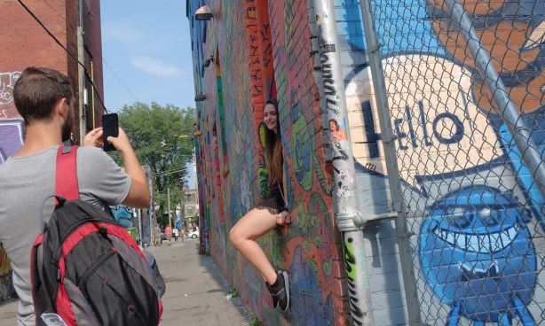 a woman sits on a window sill on a building iin Graffiti Alley as a man takes her picture 