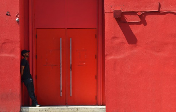 a man leans against the wall in a doorway of a building, the building is all red including the doors 