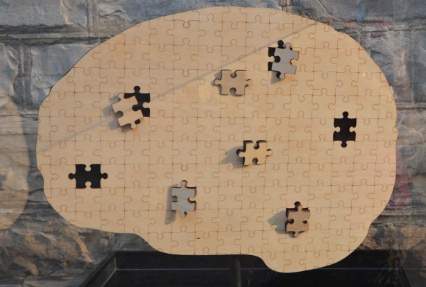 a plain brown puzzle in the shape of a brain, eight of the pieces are either missing or only partially in place