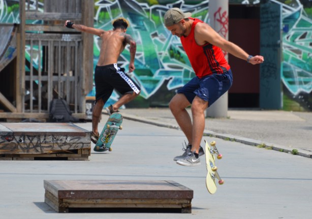 two young men skate boarding, both jumping at the same time, arm in air, 