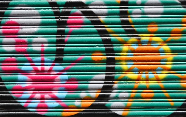 part of a painting on a metal garage door of two starburst shapes, one in pink and one in yellow 