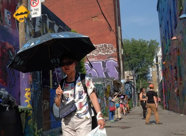 a woman carries an open blue umbrella on a sunny day as she walks down Graffiti Alley